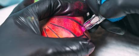 Hand mit Tätowiermaschine die ein buntes Tattoo sticht