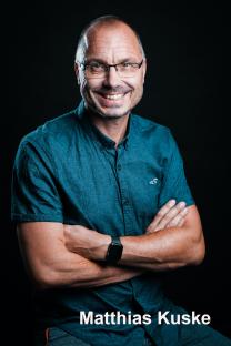 Lächelnde Person mit Brille vor dunklem Hintergrund