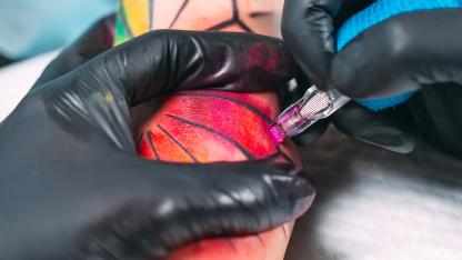 Hand mit Tätowiermaschine die ein buntes Tattoo sticht